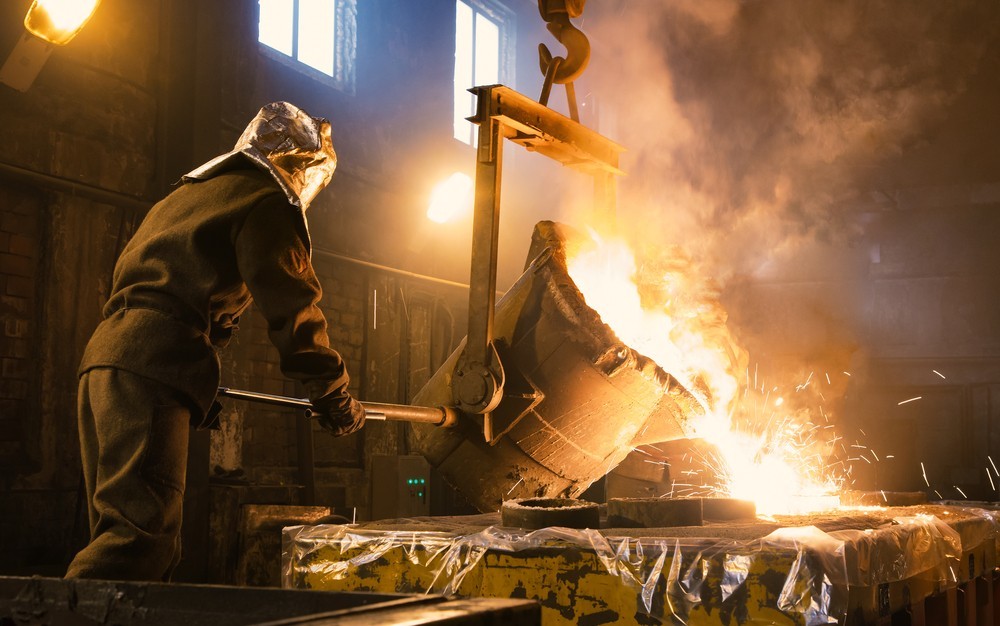 Wibest – Spot Gold Prices: A worker pouring molten metal into a mold.