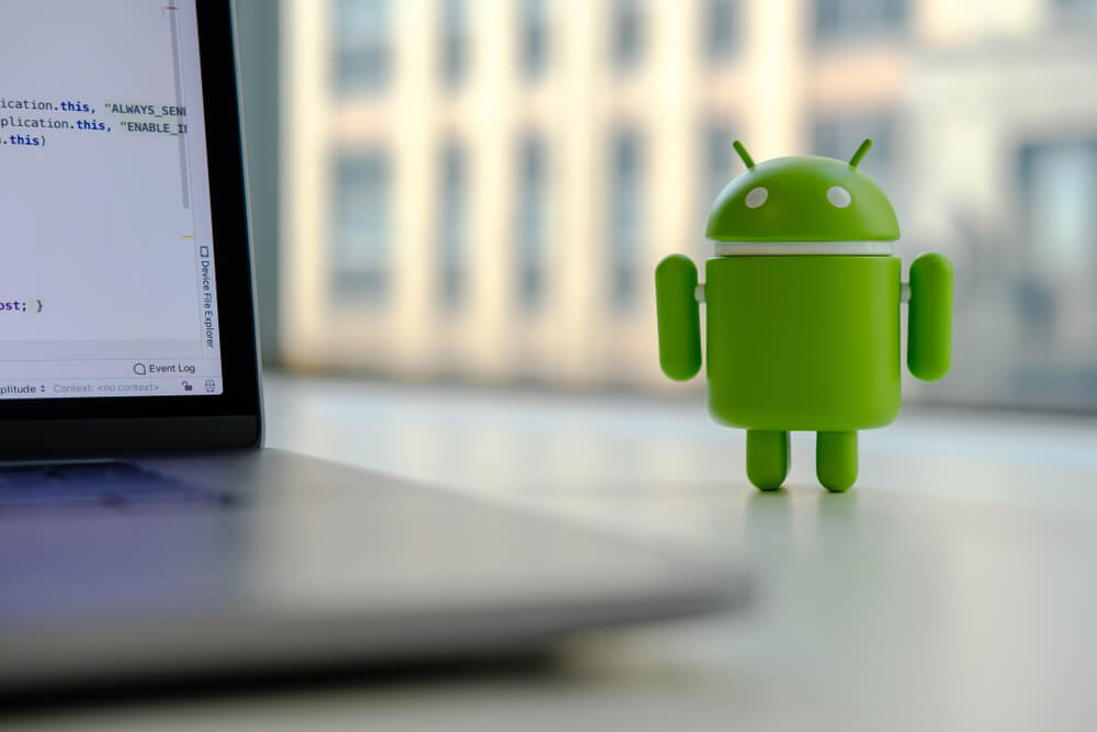 Google Android figure standing on desk near laptop computer.