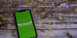Etoro on a smartphone screen on an old wooden table with leaves on it.