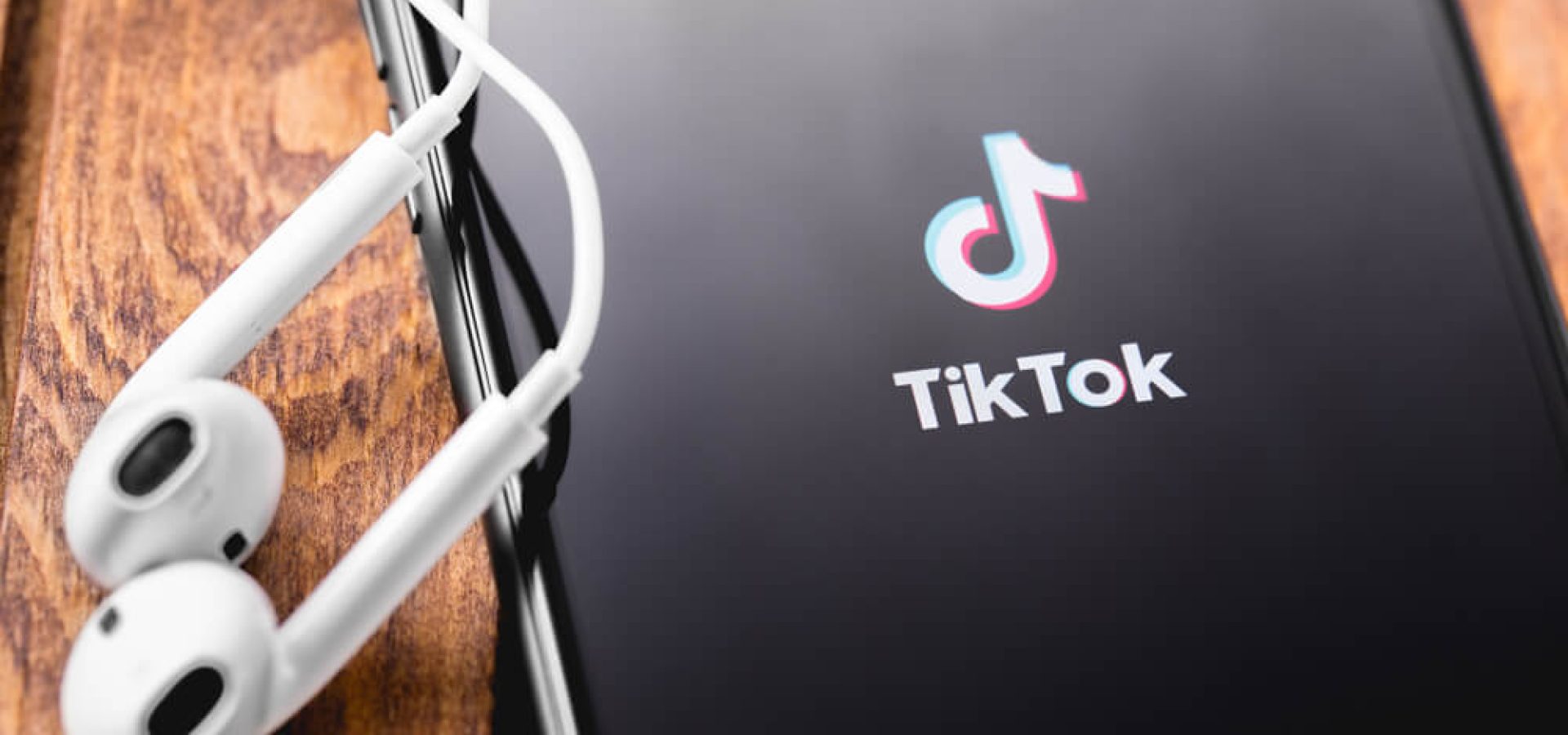 Tik Tok China: The icon of Tik Tok is shown on the screen of the phone with a pair of earpods. Wibest Broker