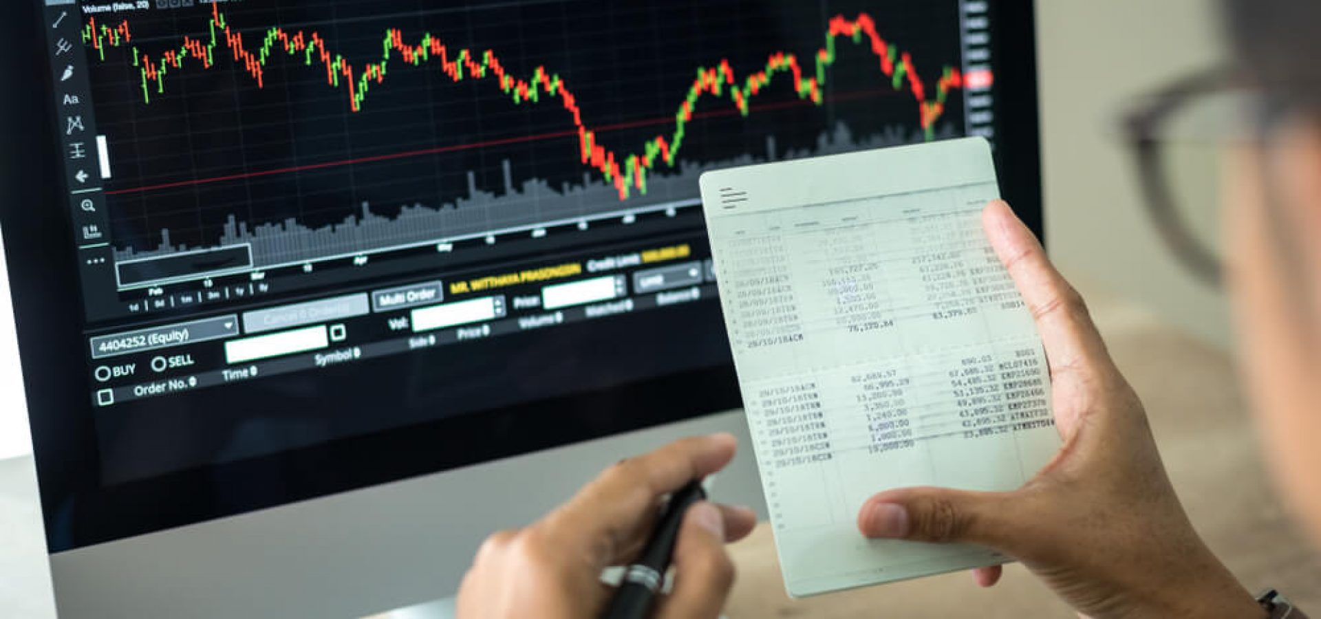 Wibest Broker- Asian Market: A hand holding a piece of paper with stocks being seen on the background.