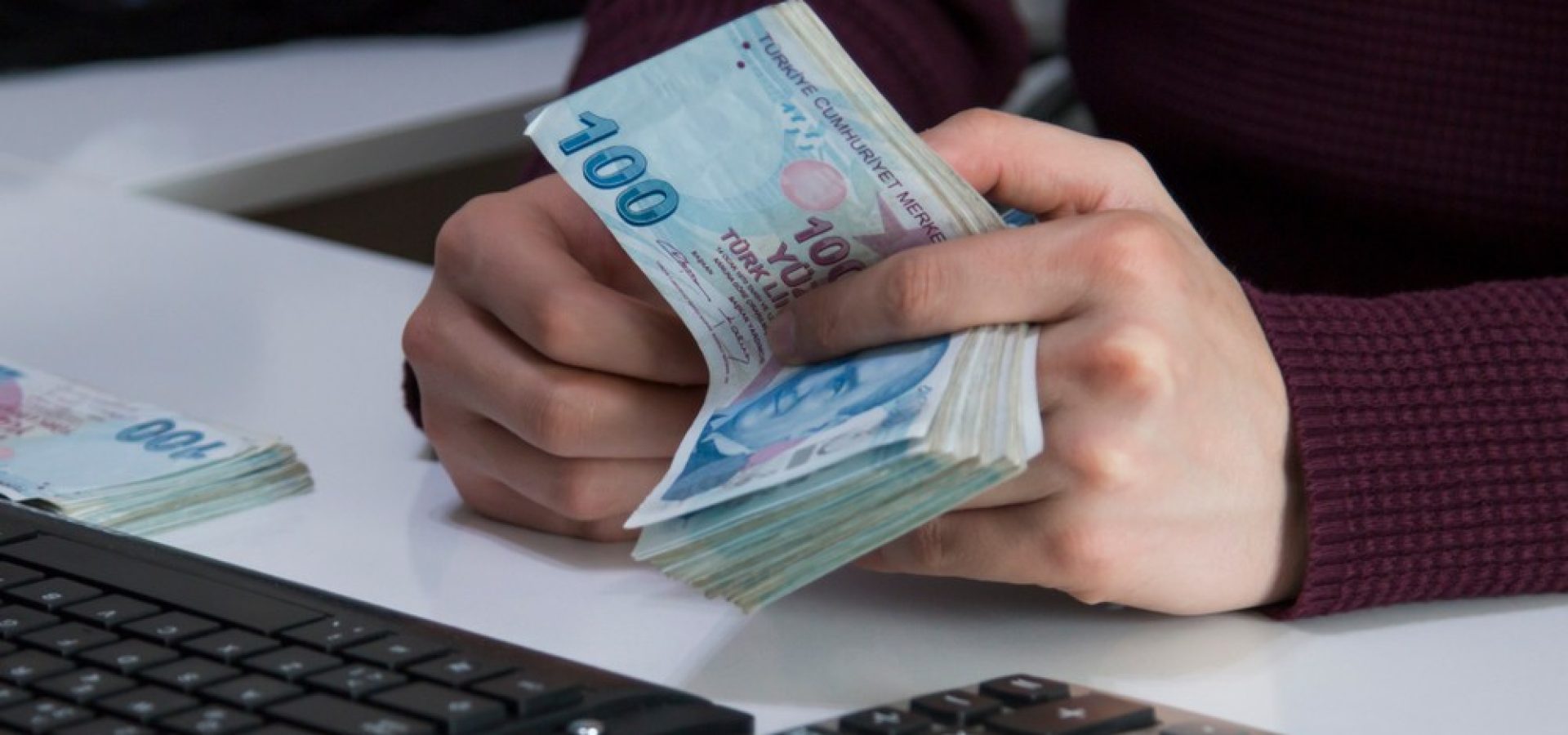 Wibest – Turkish: Hands holding Turkish lira bills in front of a keyboard.