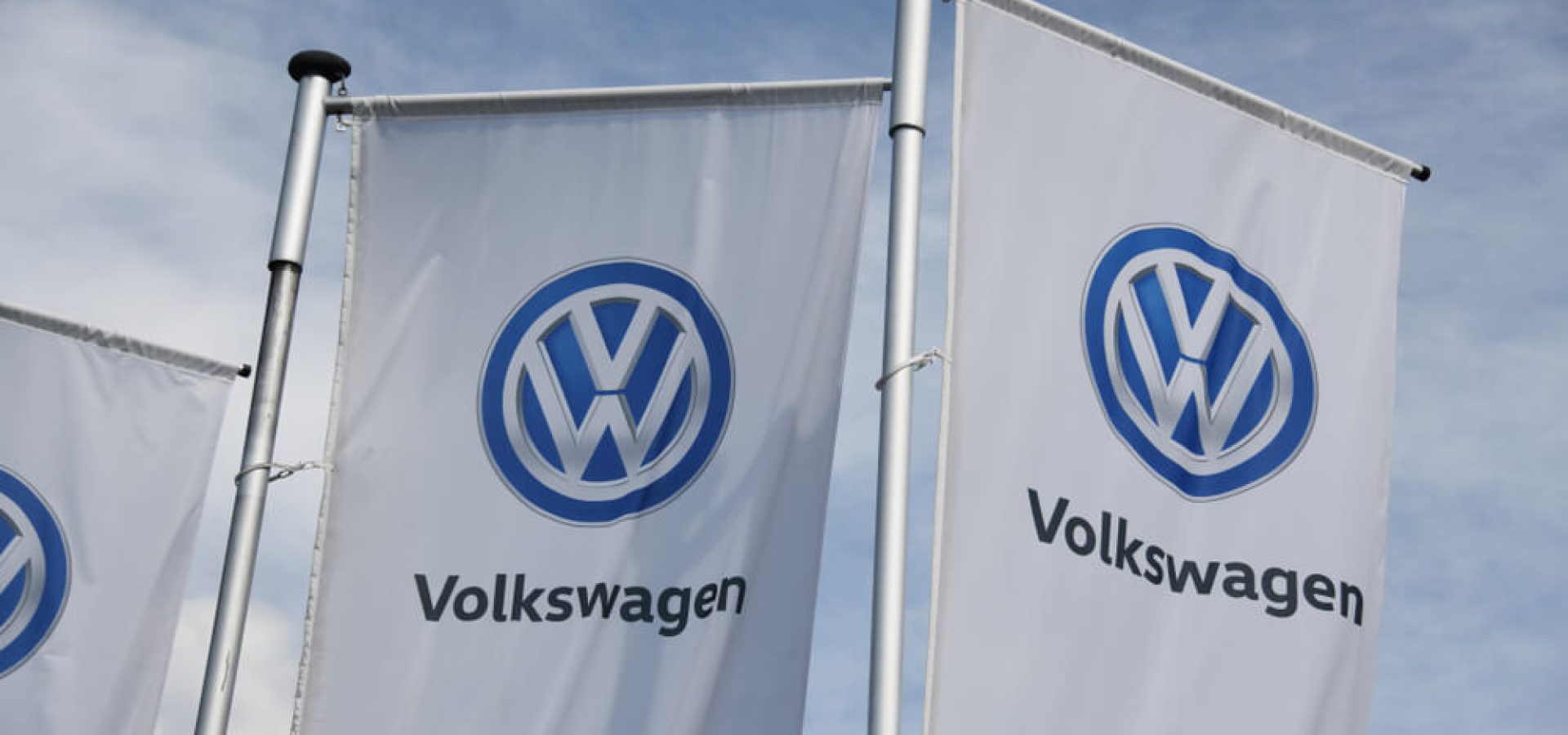 Flags with VW logo against blue sky.