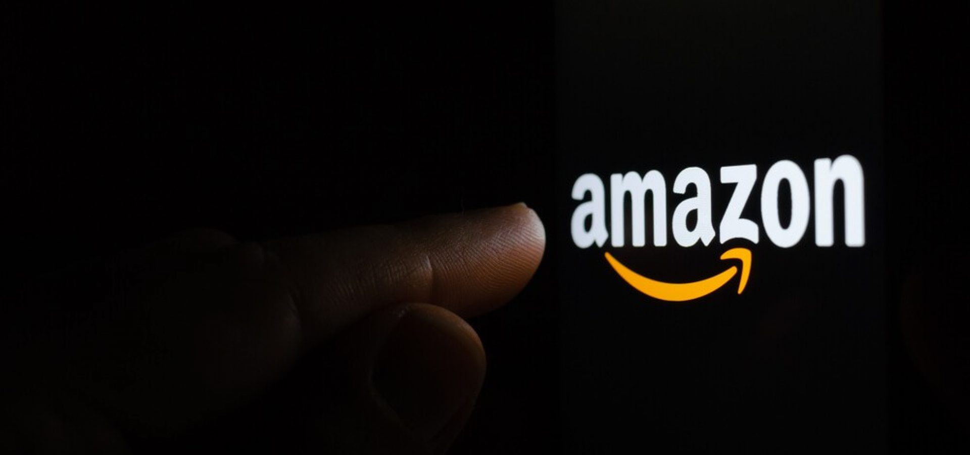 Finger touching Amazon logo on a screen in a dark.