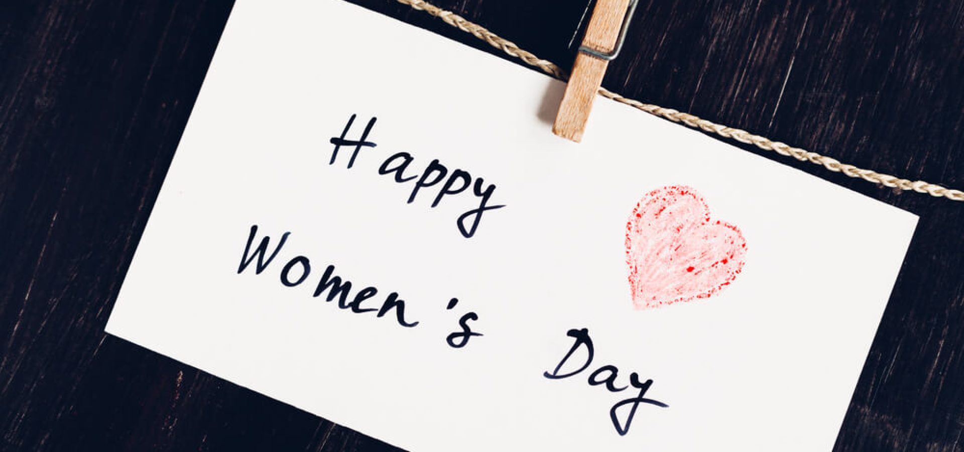 Happy Women's Day greeting message on bright white paper with red heart against a dark wooden background.