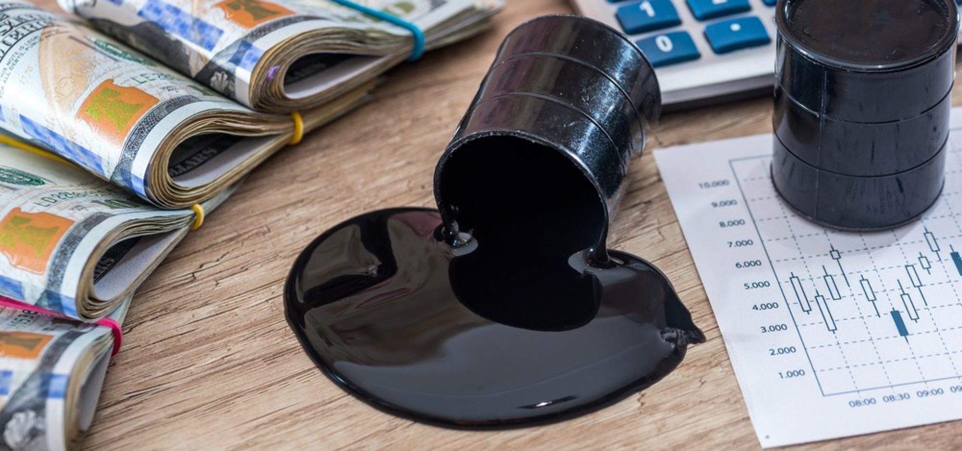 Wibest – Petroleum Crude: Crude oil barrel spilling crude on a desk with US dollar bills and a calculator.