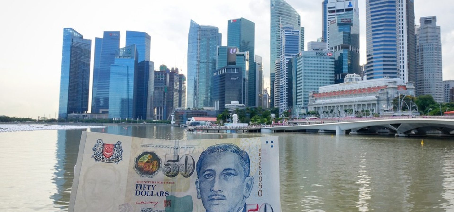 Wibest – Monetary Authority of Singapore: Singaporean dollar in held by a man and a city in the background.